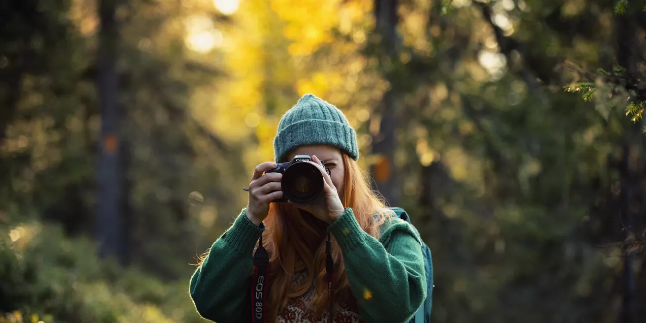 A young woman taking photos with a camera in an autumn forest