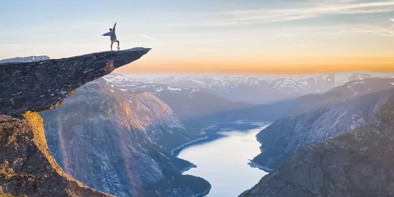 Person standing on the Trolltunga rock looking at the fjord and mountains