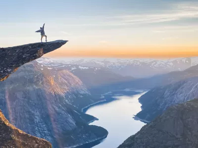 Person standing on the Trolltunga rock looking at the fjord and mountains
