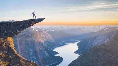 Person standing on the Trolltunga rock looking at the fjord and mountains